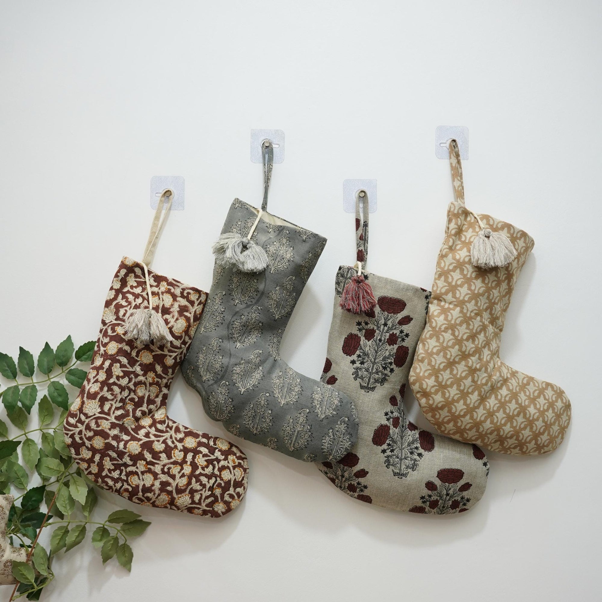 Four patterned Christmas stockings hanging on white wall with greenery.