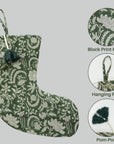 Green floral stocking with pom-pom and hanging ring on gray background.