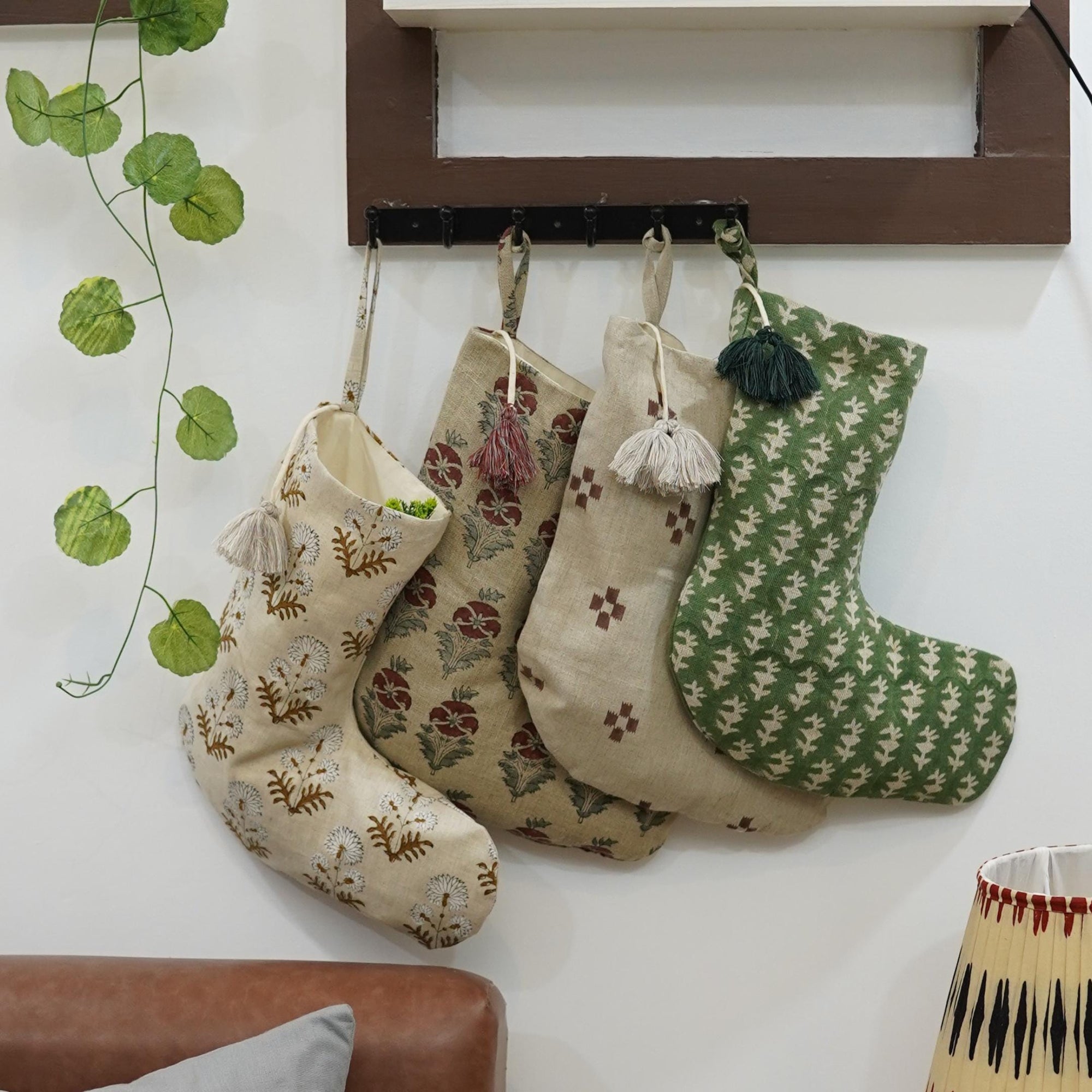 Four patterned stockings hanging on wall hook with plant and lamp in background.