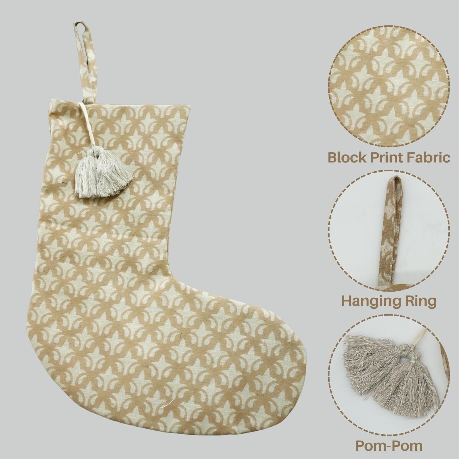 Beige Christmas stocking with block print, pom-pom, and hanging ring on gray background.