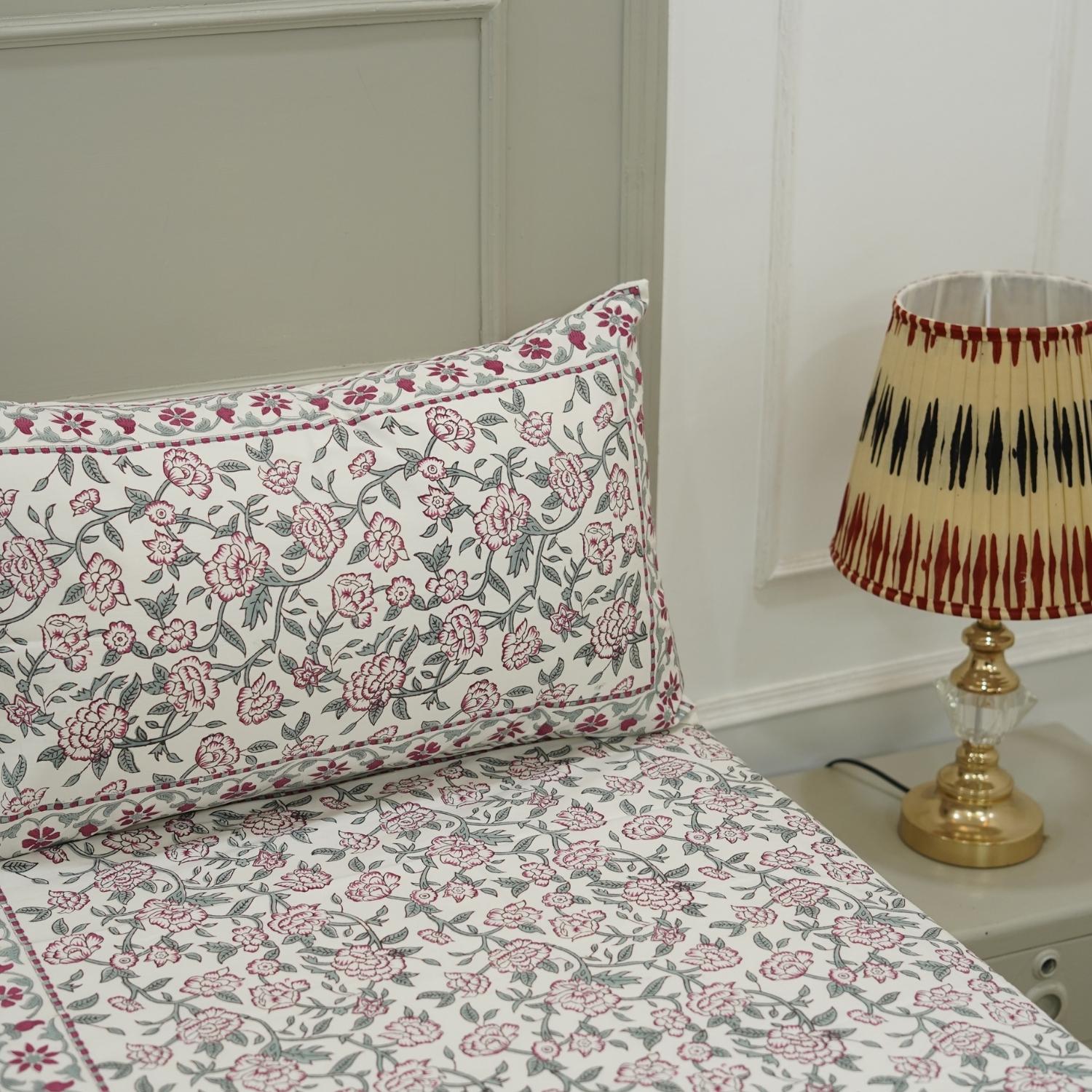 Floral-patterned pillow and bedding with a lamp on a nightstand in the background.