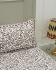 Floral-patterned pillow and bedding with a lamp on a nightstand in the background.