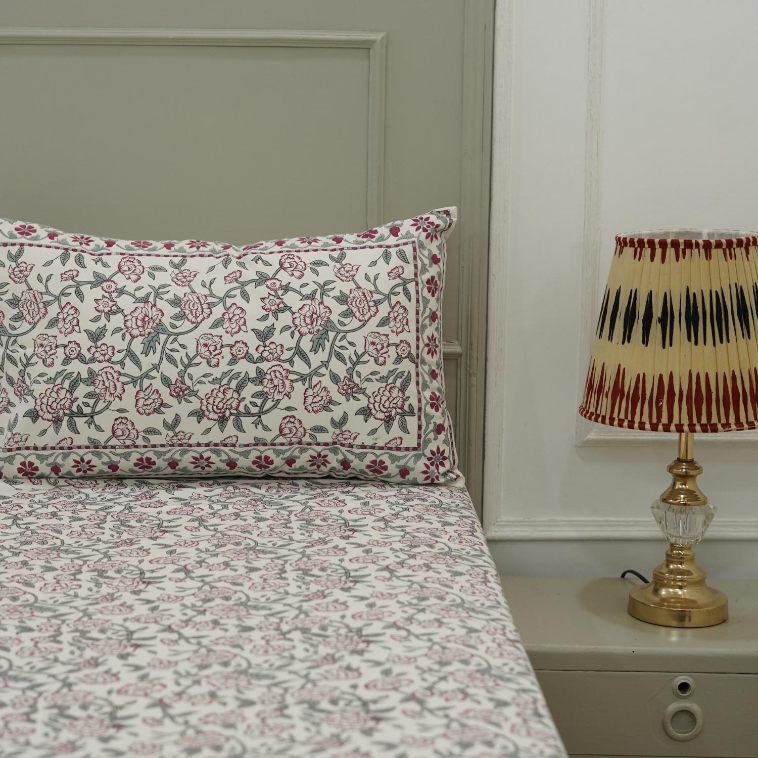 Floral patterned bedspread on a bed with a lamp on a nightstand.