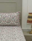 Floral patterned bedspread on a bed with a lamp on a nightstand.