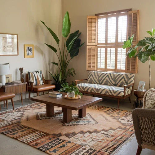 A photo of a living room with eco-chic décor. There's a large plant in the corner, a wooden coffee table, and a sofa with a geometric pattern. The walls are painted a soft beige. The floor is covered with a large rug with a tribal pattern