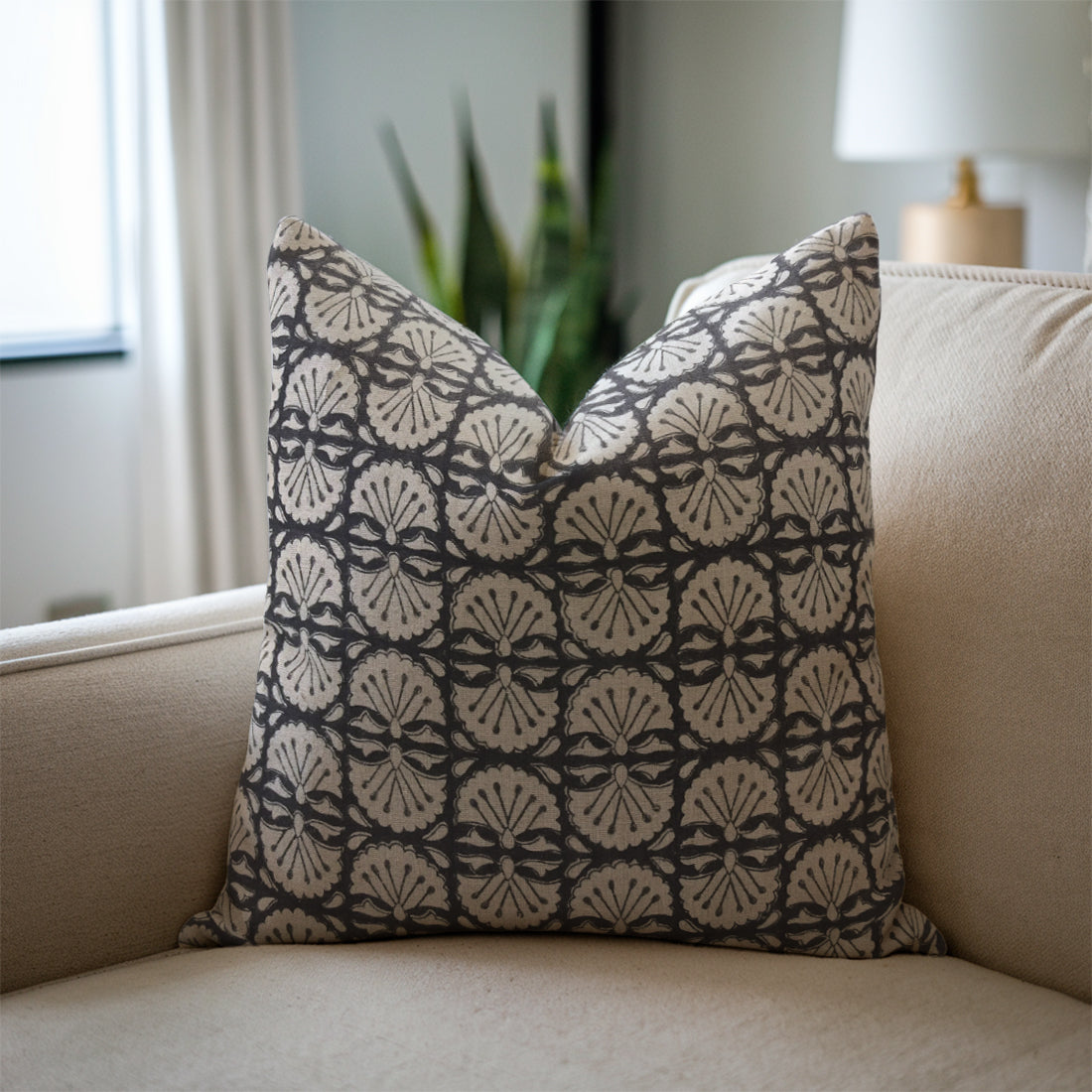 Patterned black pillow on a beige sofa with a blurred indoor background