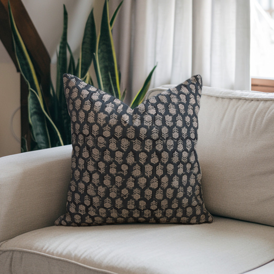 Decorative pillow with a geometric pattern on a beige sofa with plants in the background, featuring a printed cushion cover.
