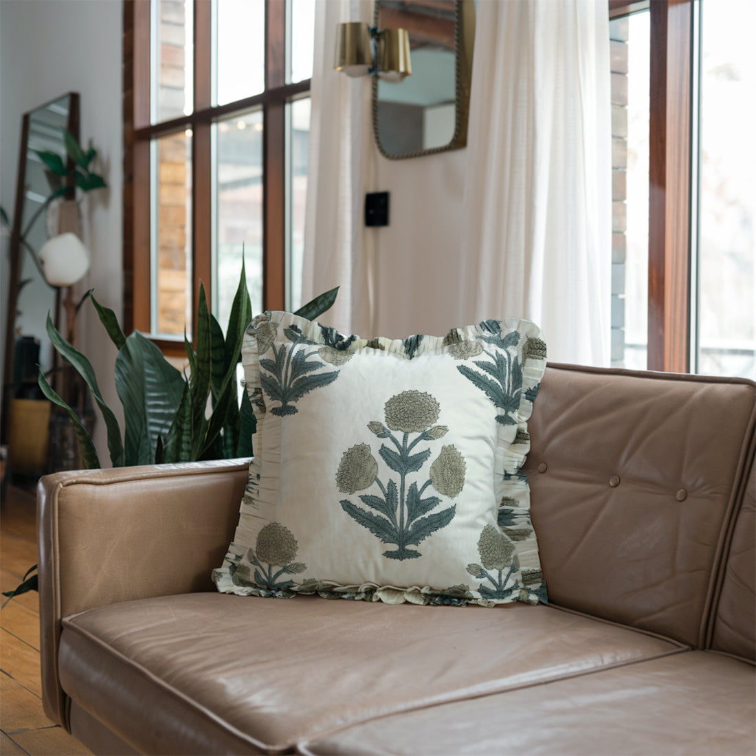 Brown leather sofa with stylish floral linen pillow covers and lush greenery.