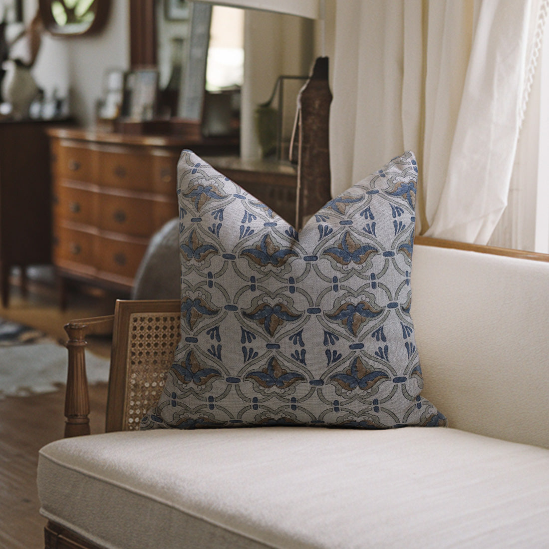 Decorative pillow with a geometric pattern on a beige sofa in a room with wooden furniture and curtains.