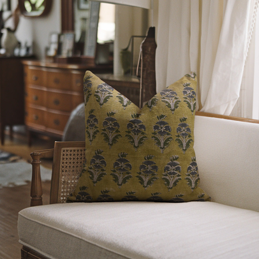 More Mukut pillow with floral pattern on a white sofa in a room with white curtains.