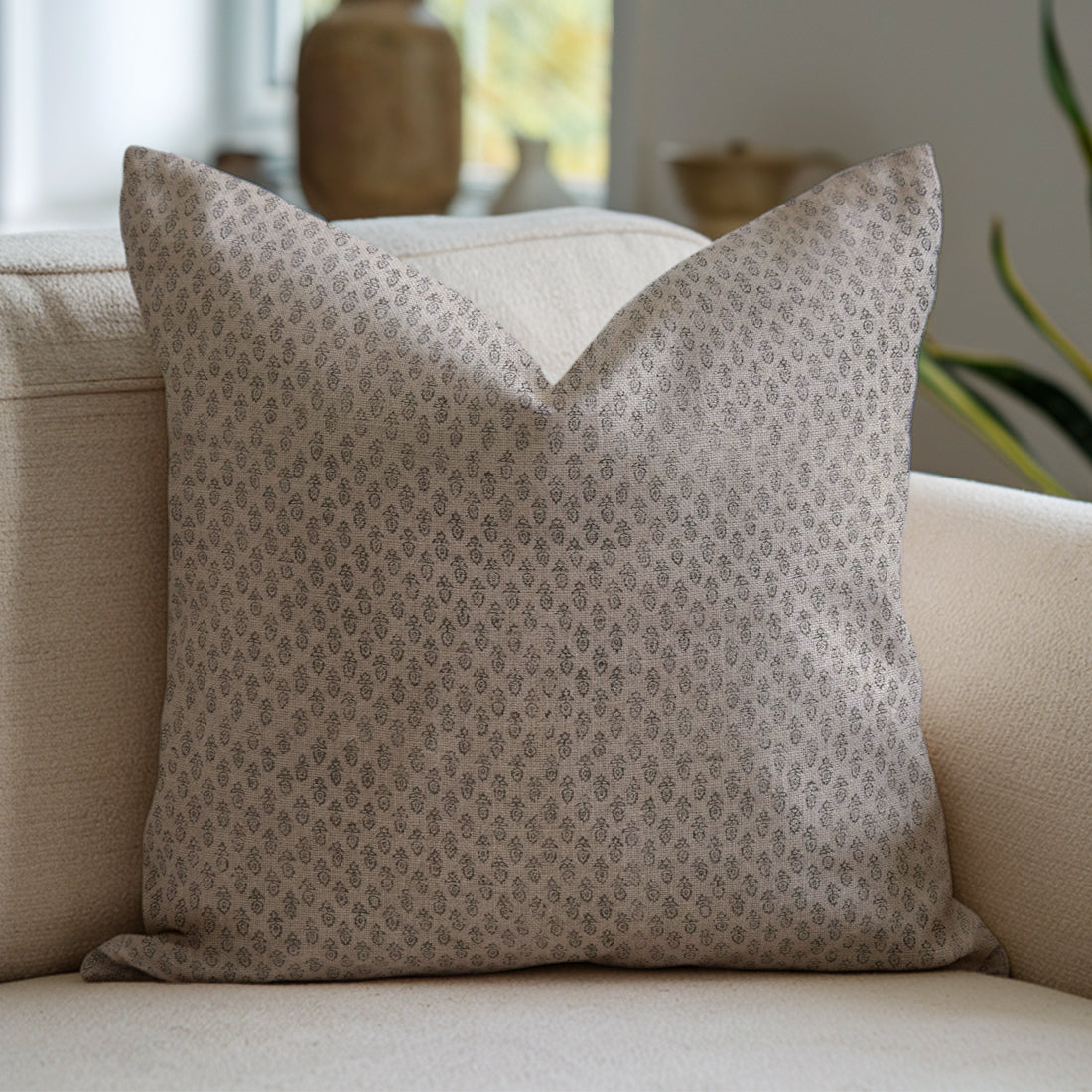 Cozy beige sofa accented with a stylish patterned pillow against a soft, blurred indoor backdrop