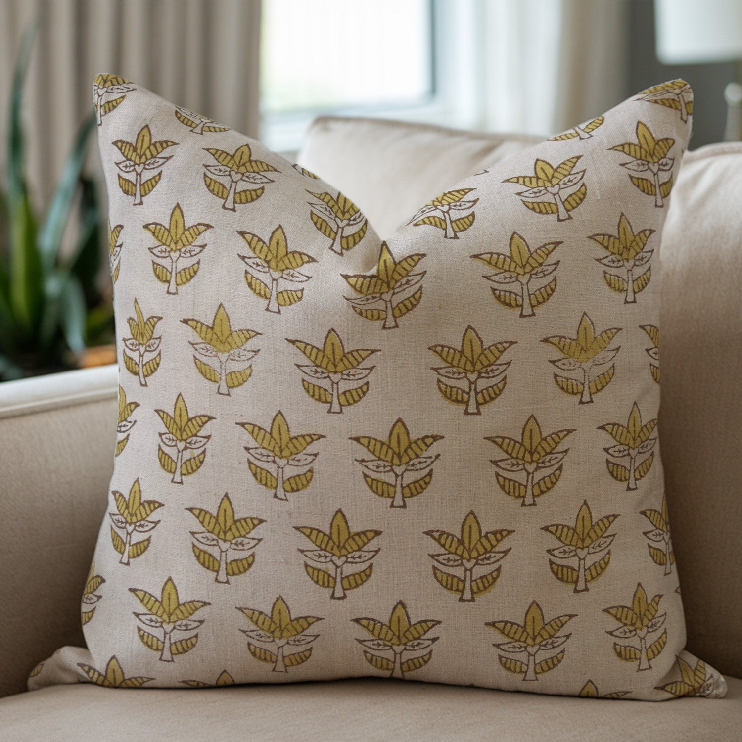 White linen pillow with yellow leaf pattern on a beige couch