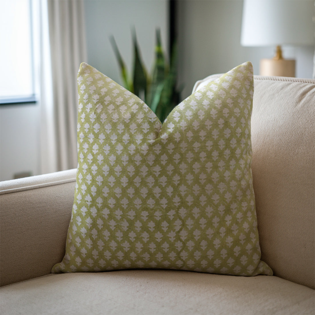 Green patterned pillow on a beige sofa with a blurred indoor background