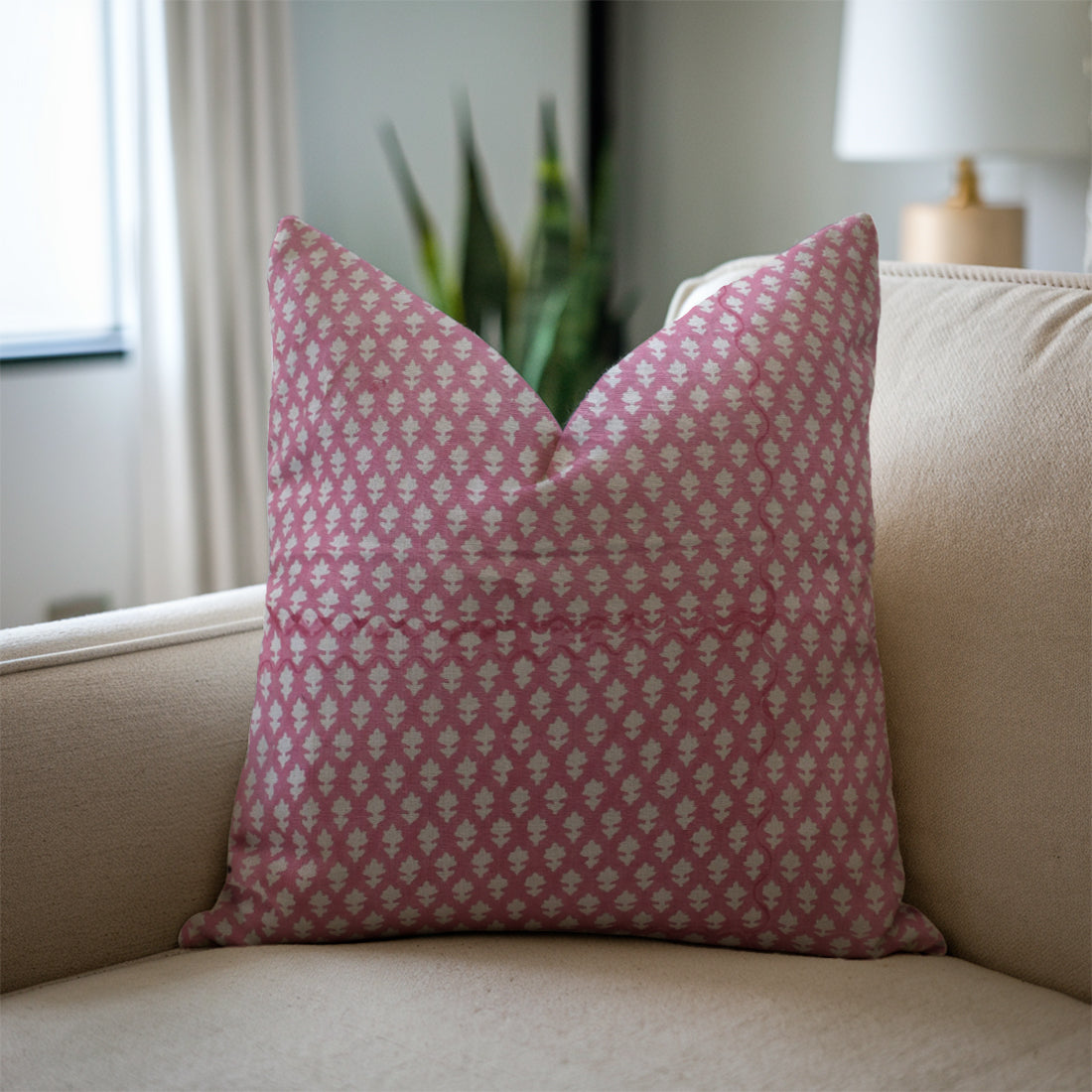 Pink patterned pillow on a beige couch with a blurred indoor background