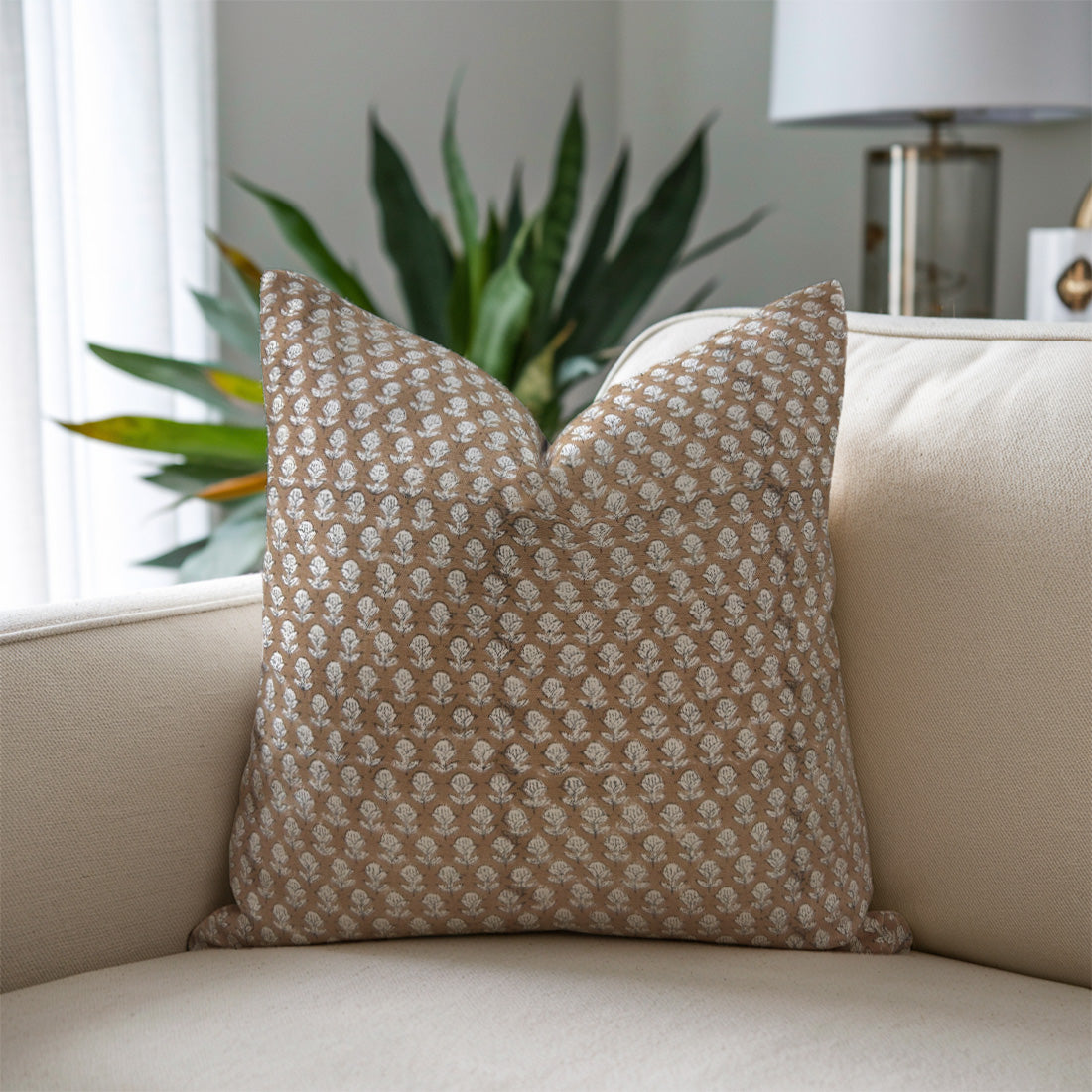 Patterned pillow on a beige sofa with a plant and lamp in the background