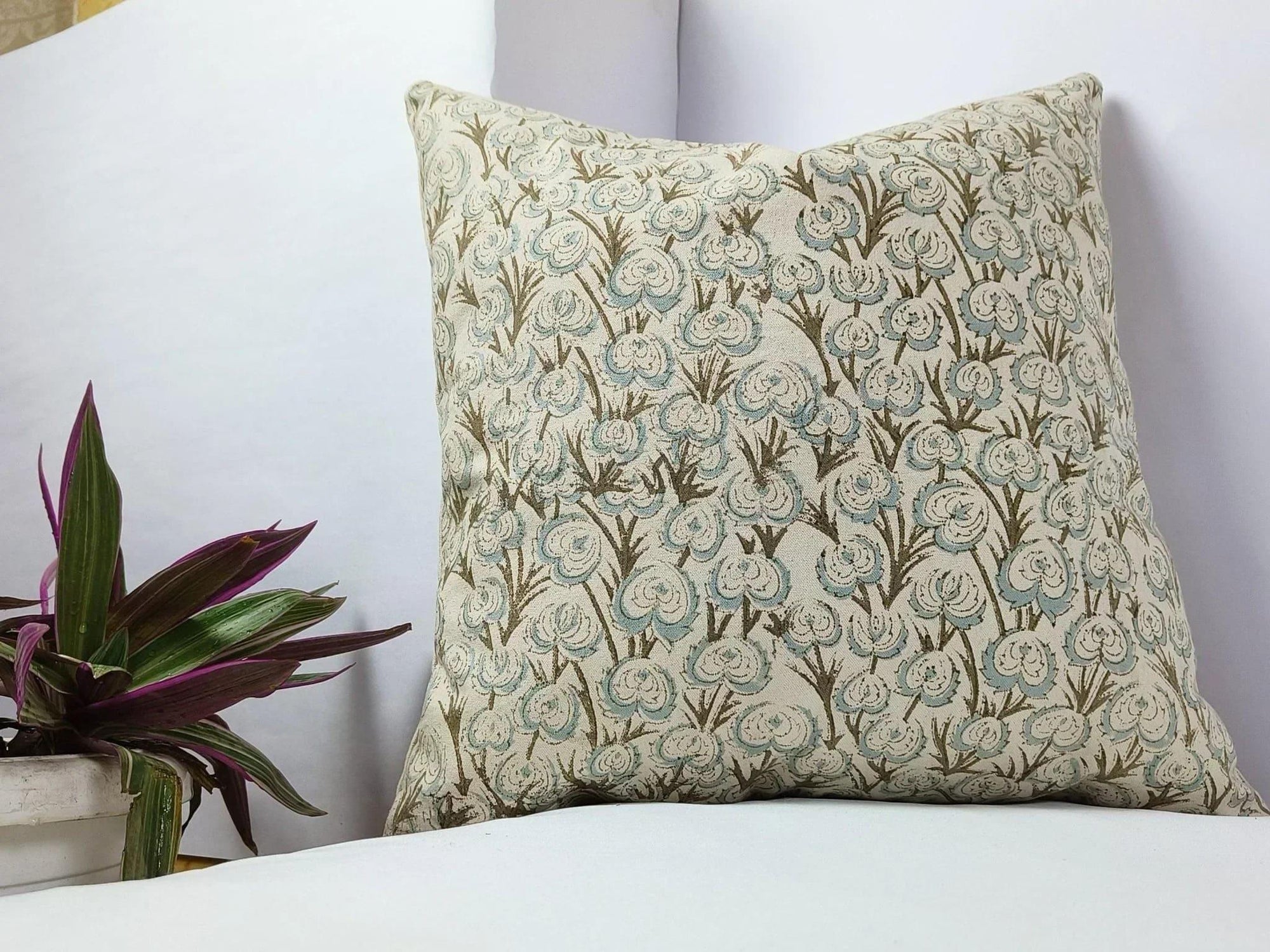 Decorative pillow with floral pattern on a white surface next to a plant