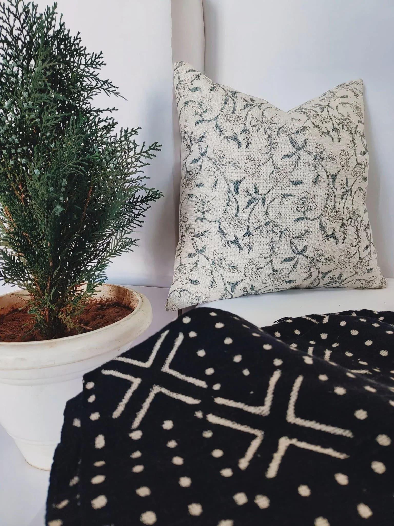 Decorative pillow with floral pattern next to a potted plant on a white surface