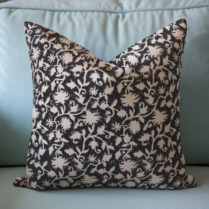 Decorative pillow with black and beige floral pattern on a light blue sofa.