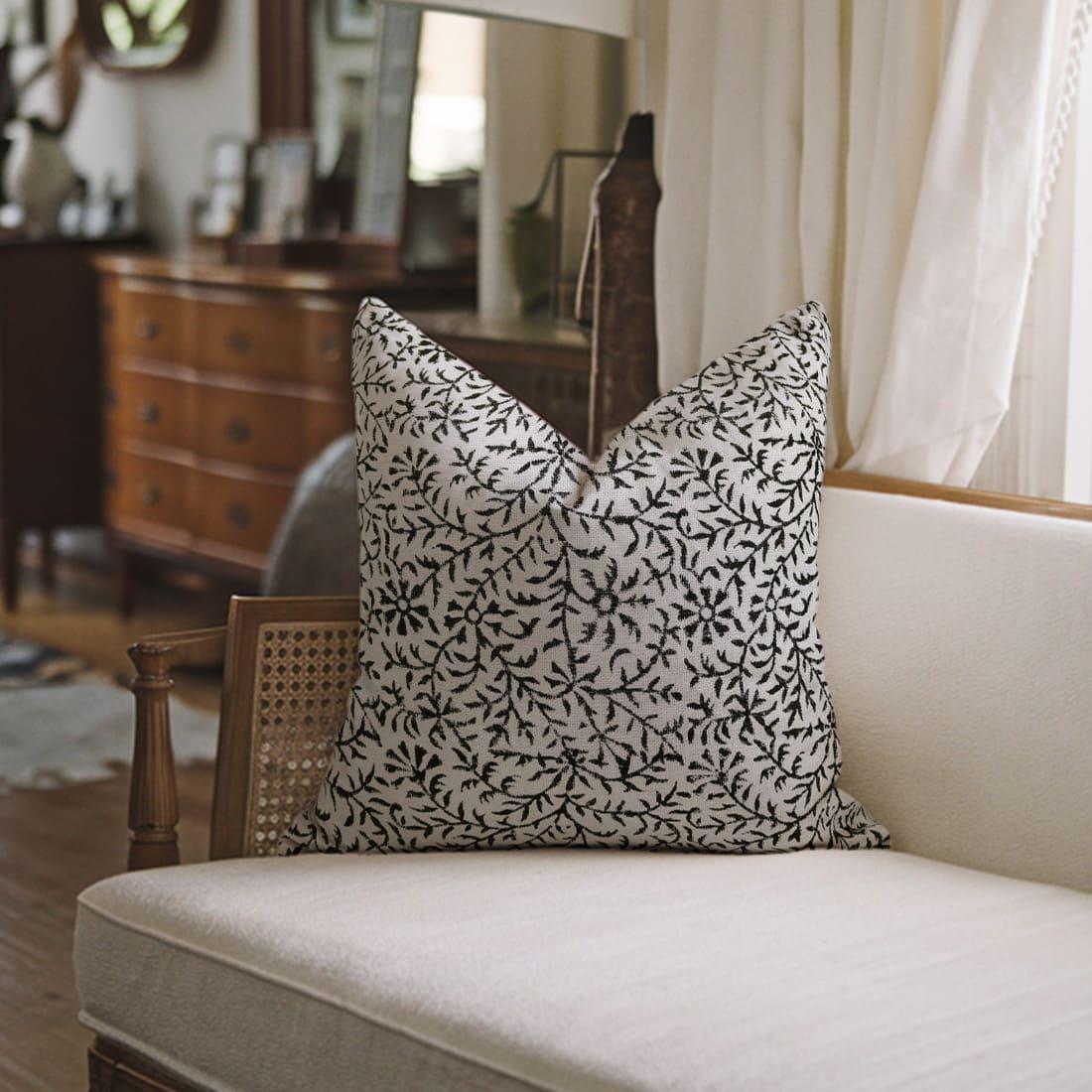 Decorative pillow with black pattern on a white sofa in a room with wooden furniture and a mirror.
