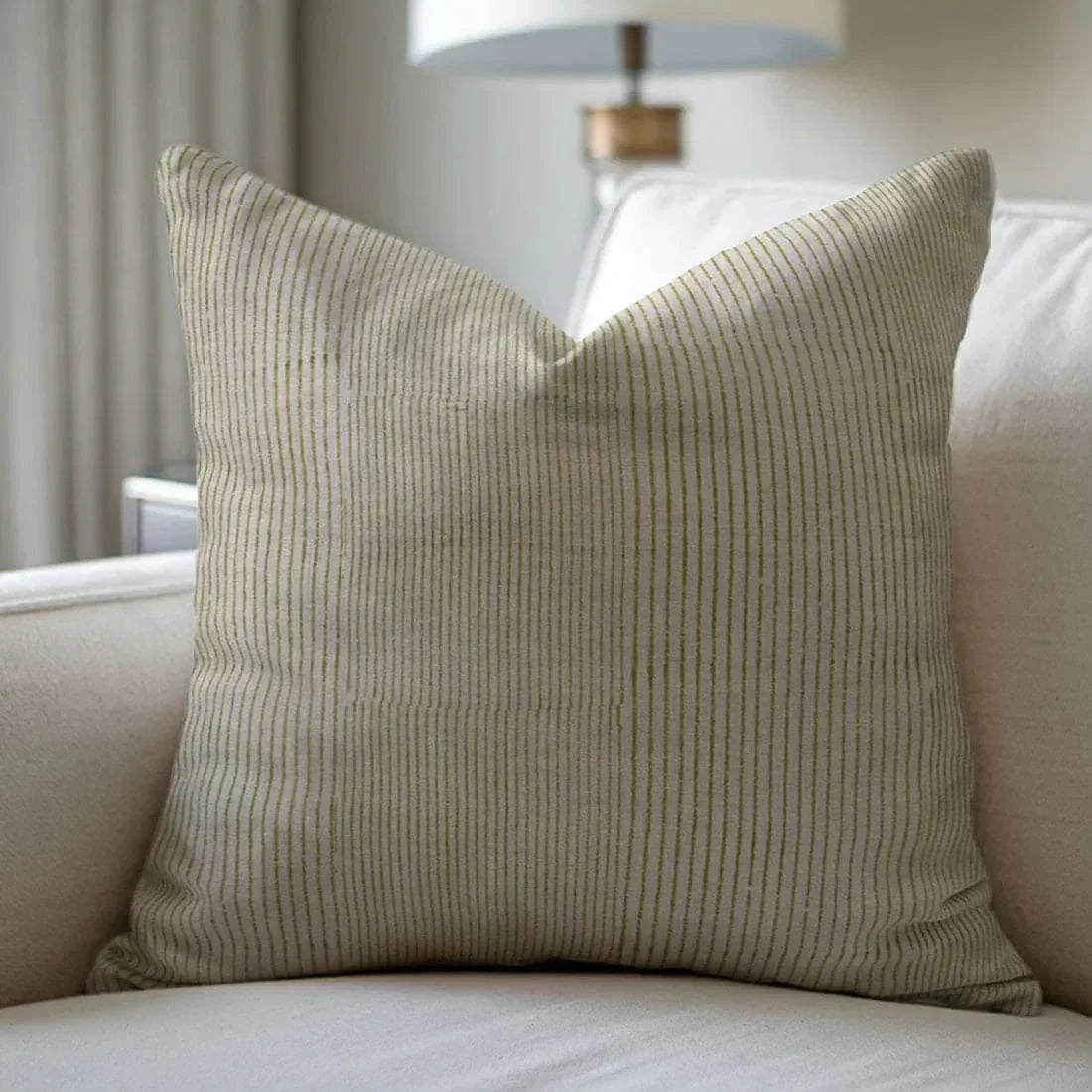 Beige ribbed pillow on a beige sofa with a blurred lamp in the background