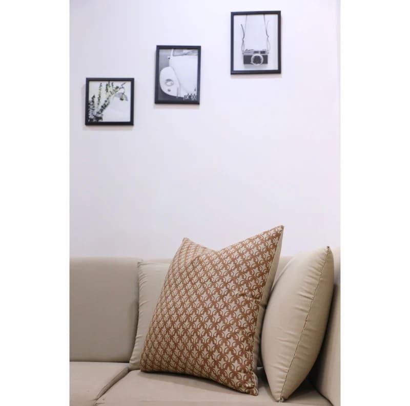 Decorative pillow on a beige sofa with framed pictures on the wall.