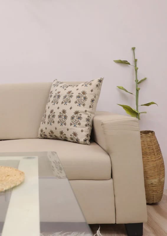 Beige sofa with a floral pillow and a plant in a room.