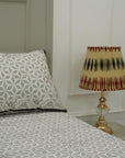Bed with patterned bedding and pillow, nightstand with lamp against a white wall.