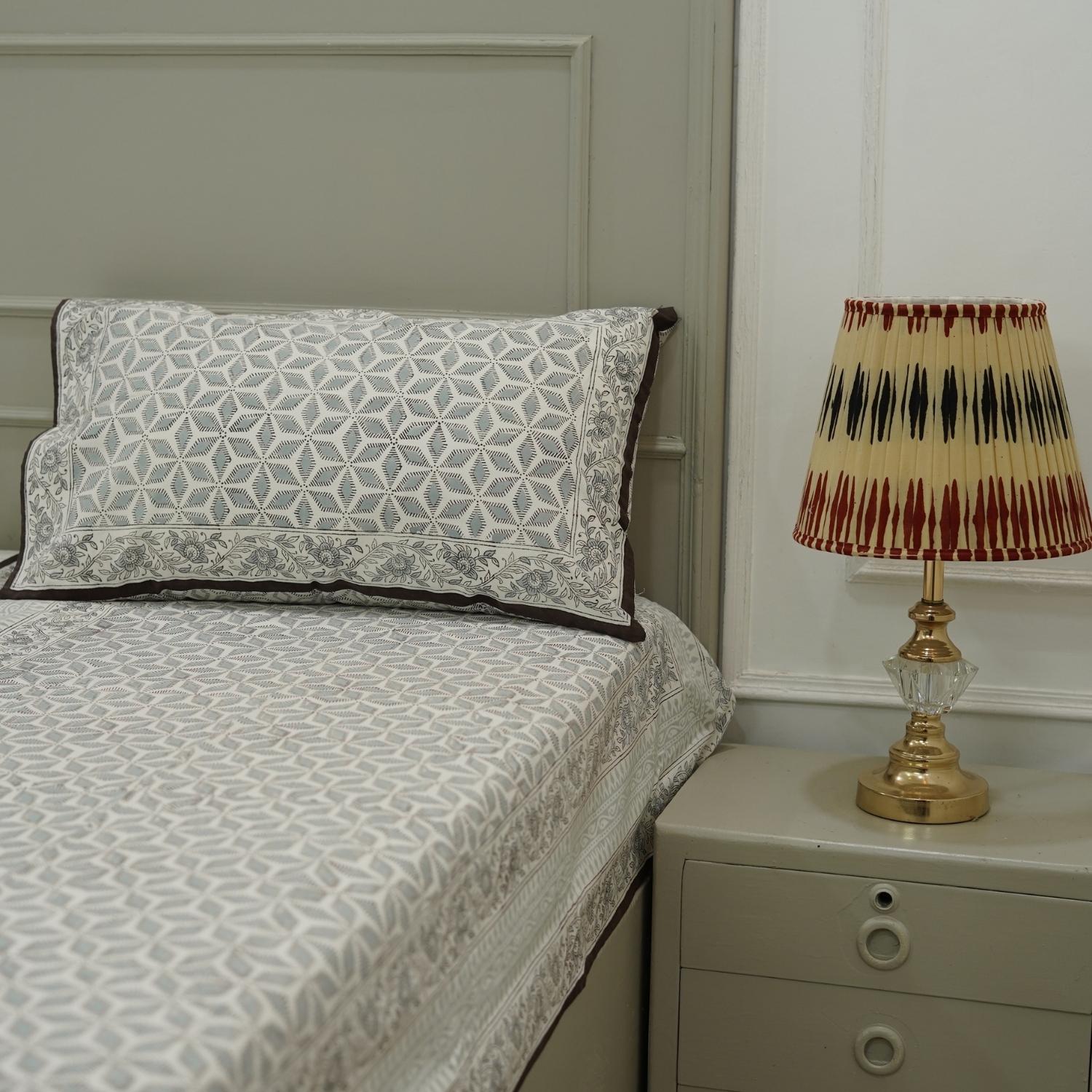 Bedsheet with patterned bedding and pillow, nightstand with lamp in a bedroom setting